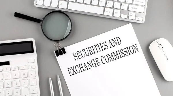 Egy íróasztalon álló papír, amelyen a Securities and Exchange Commission felirat látható, számológép és egér mellett.