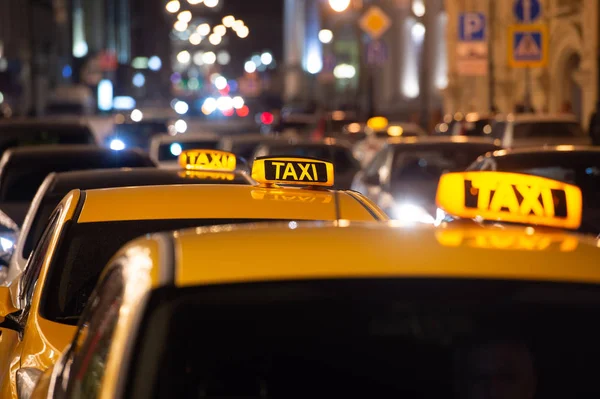 Éjszakai taxi sorban áll a város utcáján, világító TAXI feliratokkal.