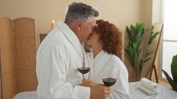 Középkorú pár romantikus pillanatot él át, borospoharakat tartva, fürdőköpenyben.
