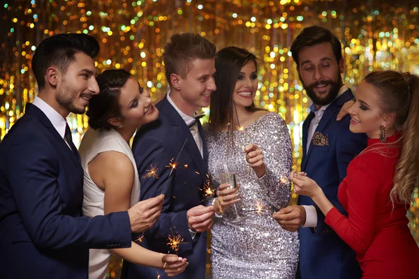 Fiatalok ünnepelnek szilveszterkor, pezsgővel és tűzijátékpálcikákkal a kezükben.