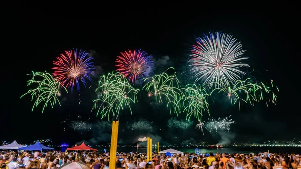 Tűzijáték a szilveszteri ünneplés közepette, sok emberrel a parton.