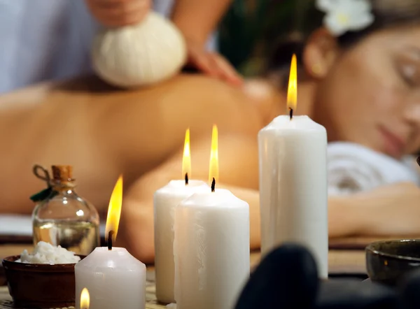 Egy fiatal nő relaxál egy wellness spa környezetében, gyertyák és olajok mellett.