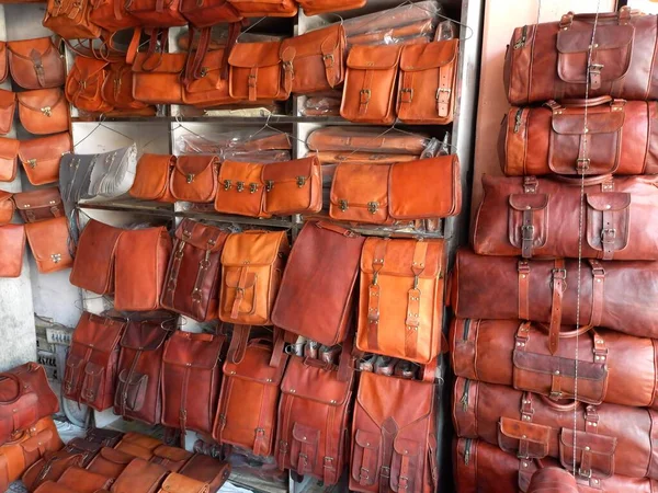 Különböző bőr táskák sorakoznak egy bolt falán, változatos árnyalatokban.